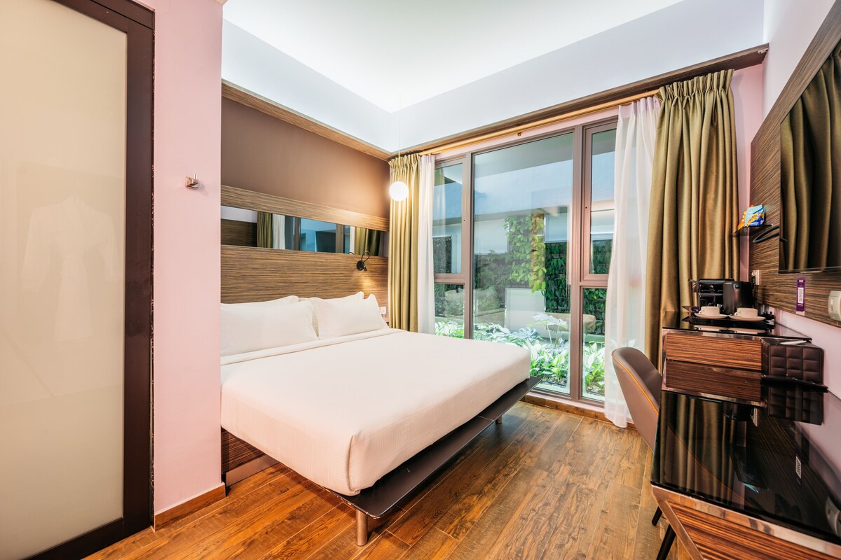 A modern hotel room with a large bed, a desk with a coffee machine, and a sliding glass door to a balcony.