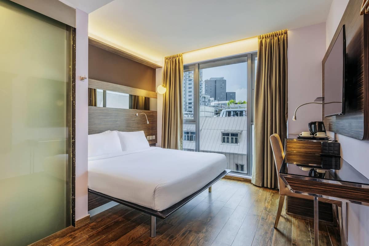 Une chambre d’hôtel équipée d’un lit, d’un bureau, d’une chaise, d’une télévision et d’une grande fenêtre avec des rideaux.
