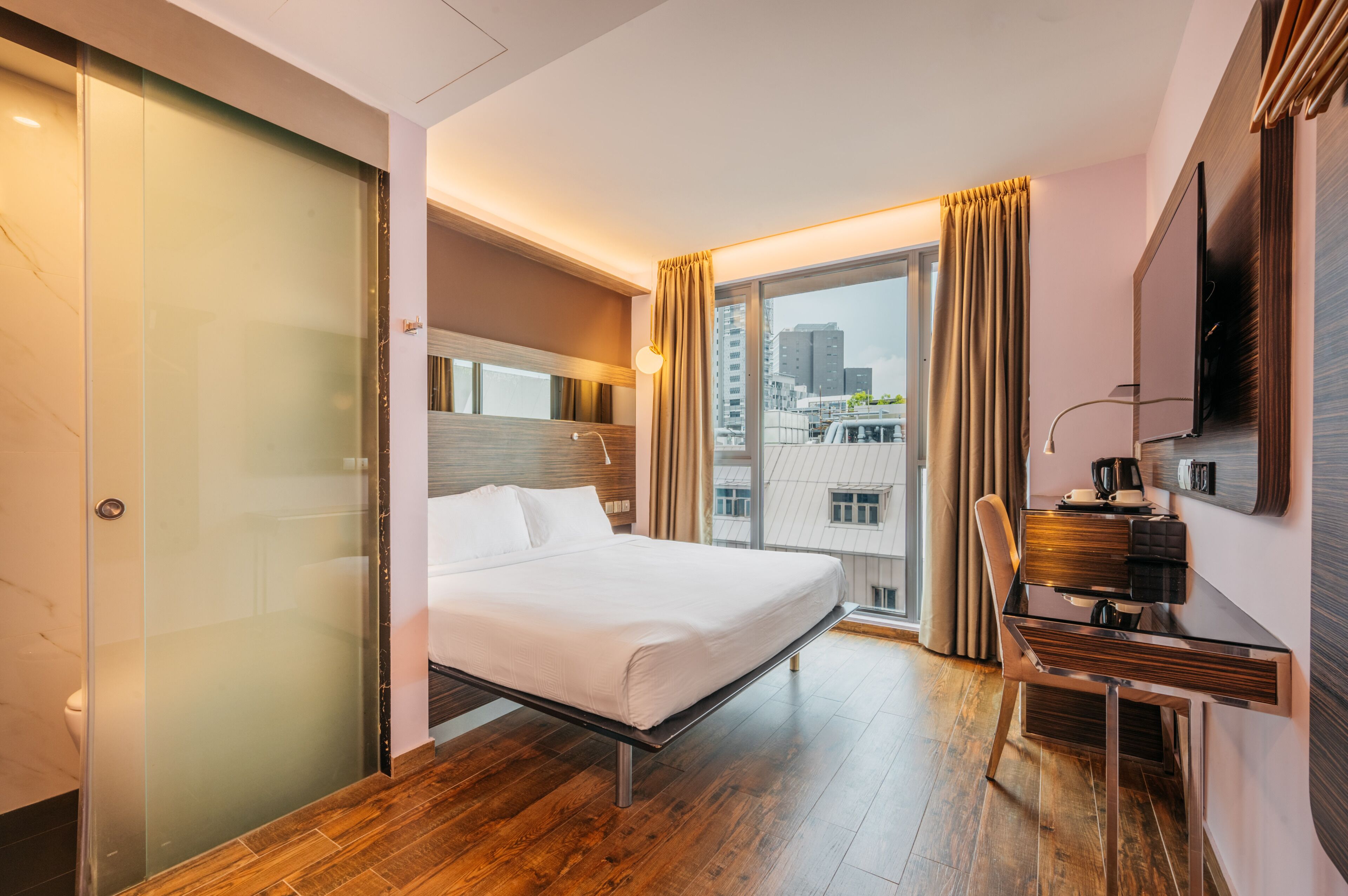 Quarto de hotel moderno com cama, escrivaninha e uma janela grande com cortinas.