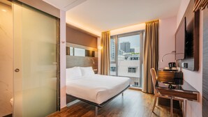 Una habitación de hotel moderna con cama, escritorio y un ventanal con cortinas.