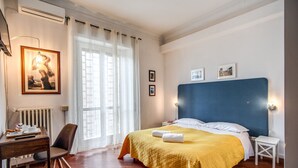 Habitación de hotel con una cama grande, un escritorio con silla, un radiador y una ventana con cortinas.