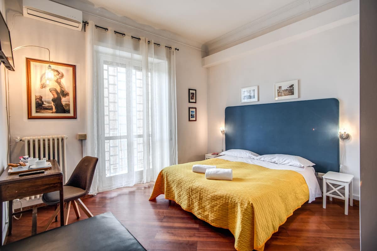 Habitación de hotel con una cama grande, un escritorio con silla, un radiador y una ventana con cortinas.