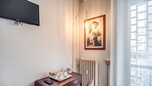 Una habitación con escritorio de madera, una silla, un cuadro enmarco, un radiador y una ventana con vistas.