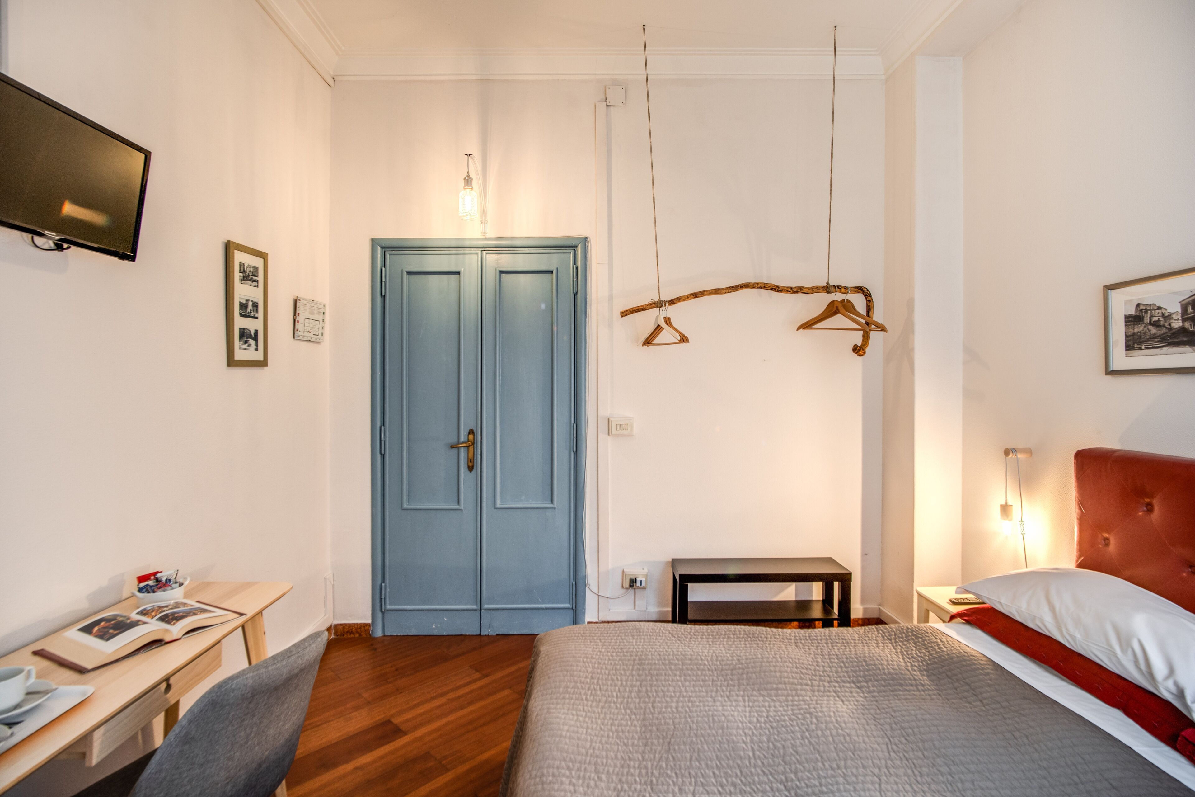 Een slaapkamer met een bed, een bureau, een stoel, een blauwe deur en een televisie aan de muur.