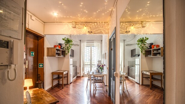 Un pasillo con piso de madera, un comedor con mesa y sillas, y una zona de cocina con armarios y un refrigerador.