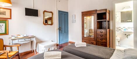 Habitación de hotel con dos camas, un escritorio, una silla, un armario, televisión y un baño visible a través de una puerta abierta.