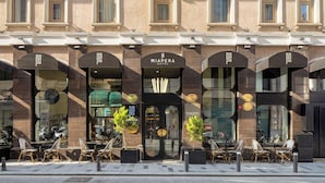 The exterior of the Miapera Hotel with a classic facade, large windows, and outdoor seating area.