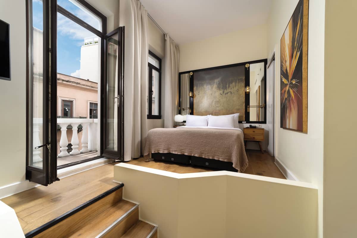 A bedroom with a bed, a nightstand, a painting, and a view through an open window.
