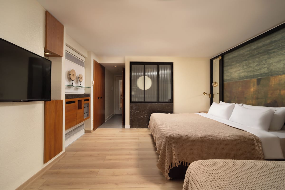 A hotel room with a bed, a TV, a wooden cabinet, and a painting on the wall.