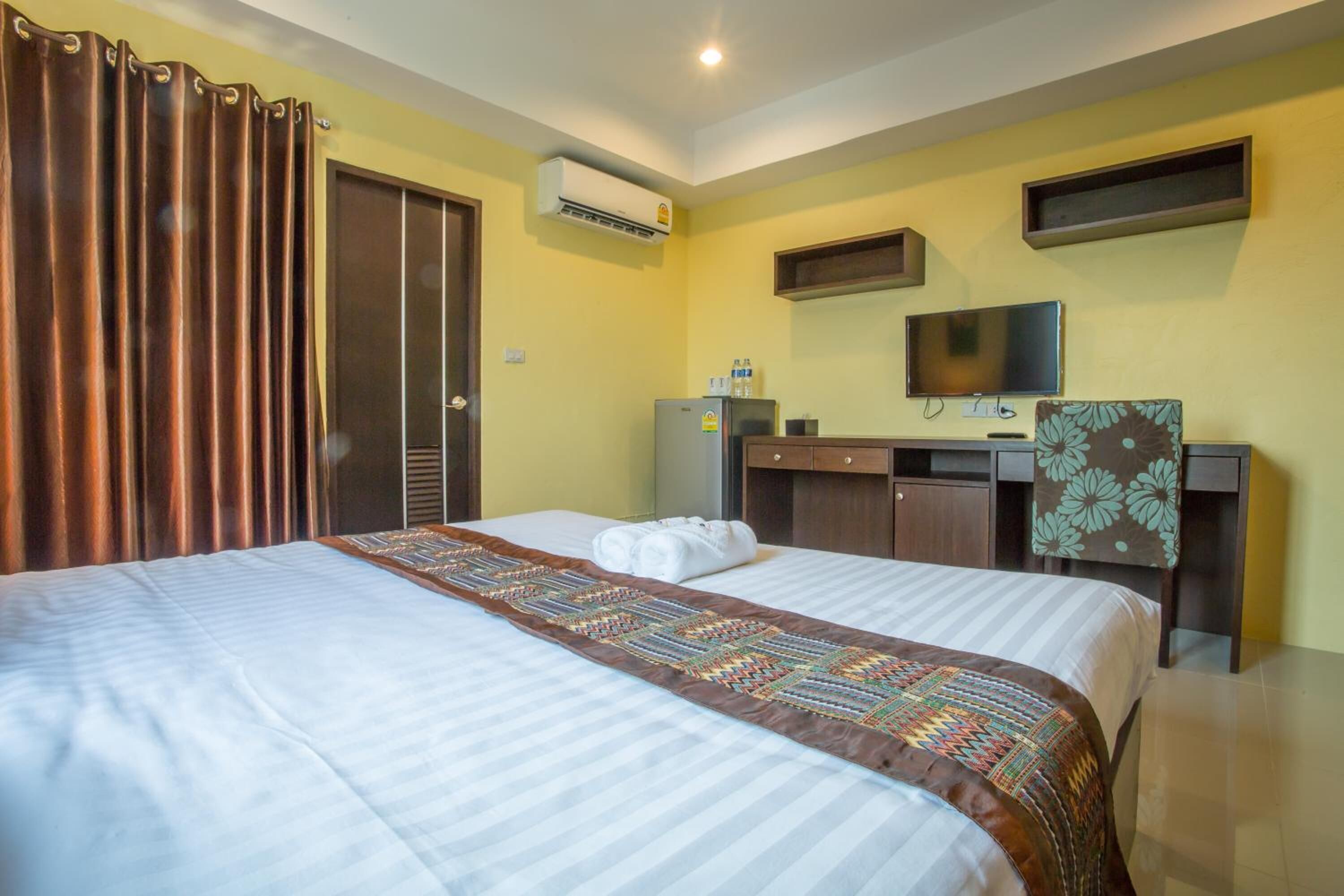 A hotel room with two beds, a desk with a television, a wardrobe, and an air conditioning unit.