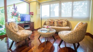 A living room with wicker furniture, a television, and a window with blinds. - TL Residence (Chiang Mai)