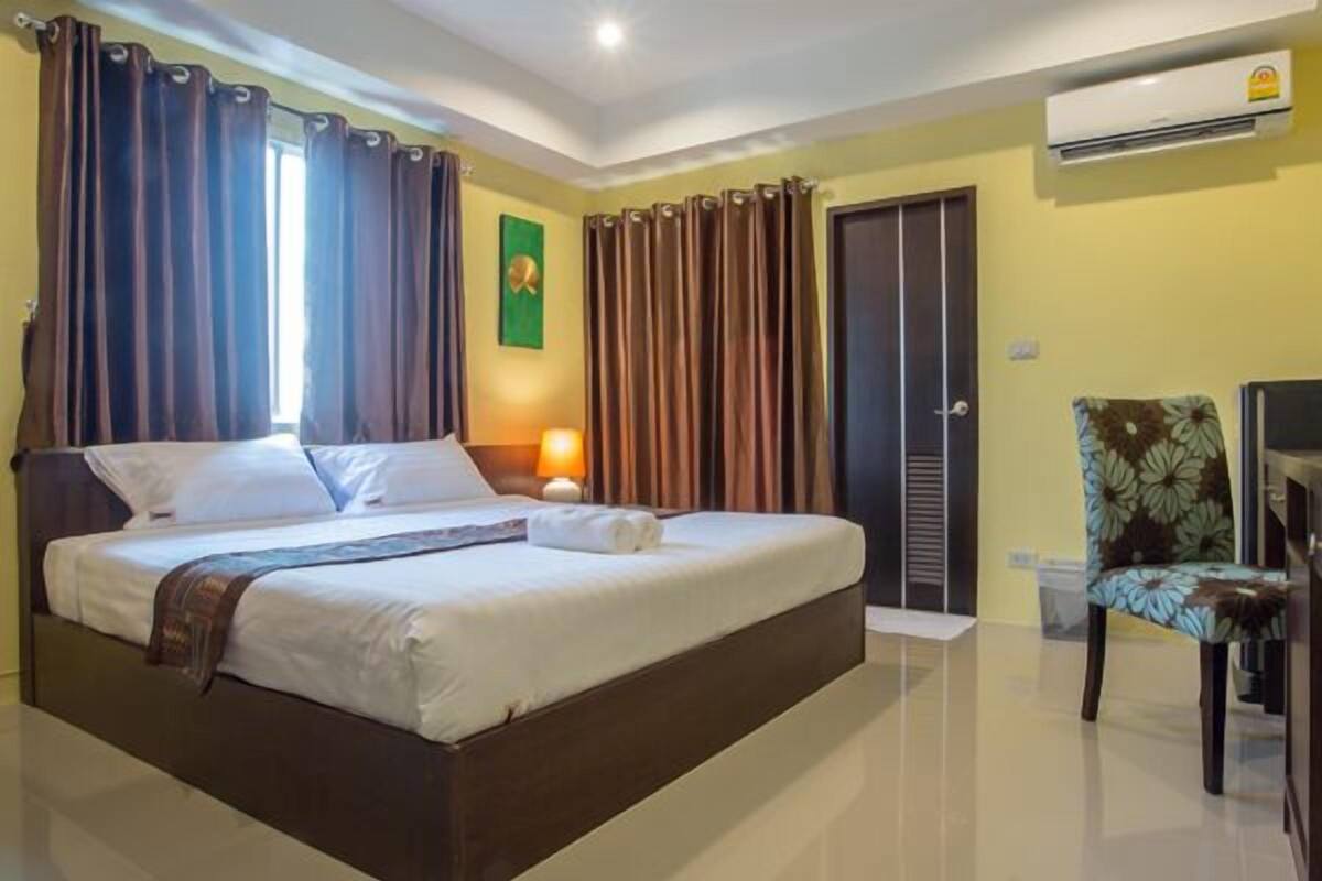 Habitación de hotel con una cama grande, cortinas, un escritorio, una silla y un equipo de aire acondicionado.