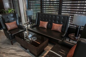 Una sala de estar moderna con un sofá de cuero negro, dos sillones y una mesa de centro de vidrio.