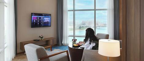 Habitación de hotel con un ventanal grande, televisor de pantalla plana, mesa de comedor y sofá.
