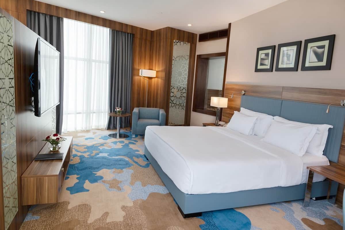 A hotel room with a large bed, a desk, a chair, a TV, and a window with curtains.