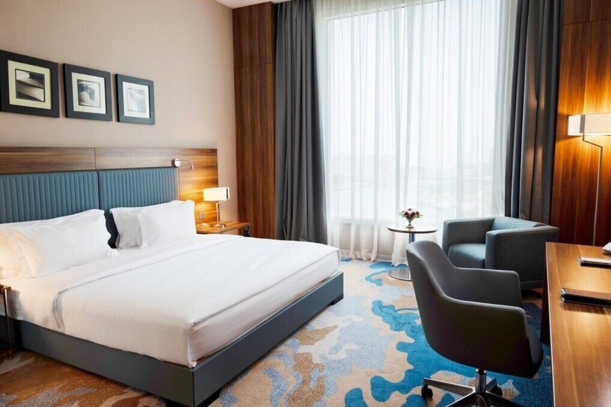A hotel room with a large bed, a desk, a chair, a small table, and a window with curtains.
