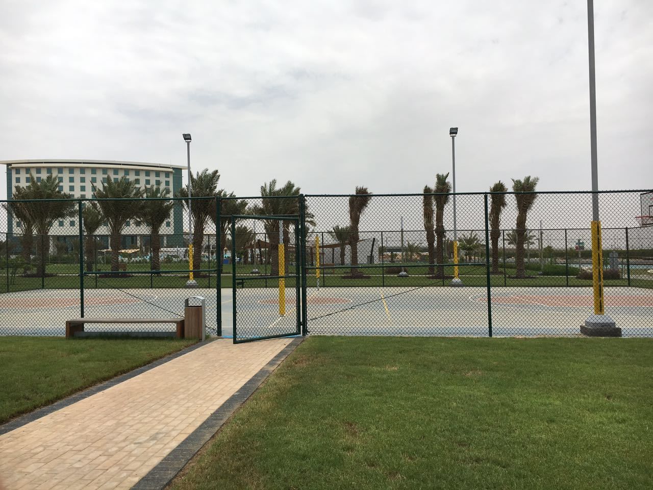 Un espacio al aire libre cercado con un sendero pavimentado, bancos y palmeras.