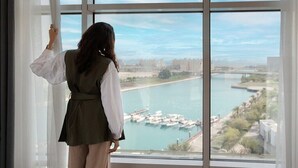 A person standing by a large window overlooking a marina with boats and a river. - Bay La Sun Hotel & Marina (Rabigh)