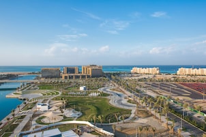 Una zona costera urbana con edificios modernos, un puerto deportivo y un parque ajardinado.