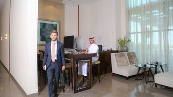 A man in a suit walking through a hotel lobby with a desk, computer, and a sofa.