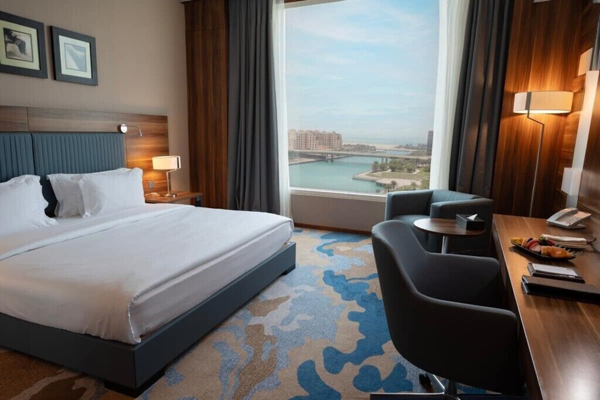 Une chambre d’hôtel avec un grand lit, un bureau avec une lampe, une chaise et une vue sur le paysage urbain.