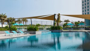 A swimming pool with lounge chairs and umbrellas, surrounded by greenery and a tall building in the background. - Bay La Sun Hotel & Marina (Rabigh)