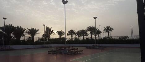 An outdoor tennis court with benches and palm trees.