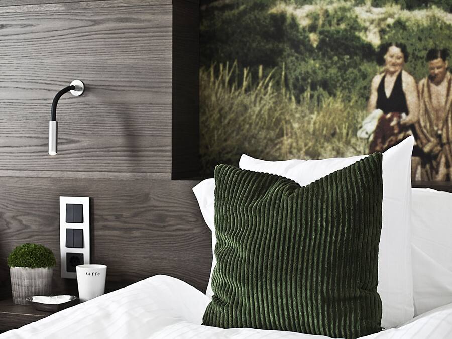 Un dormitorio moderno con cabecera de madera, una mesita de noche con una planta y una taza, y un cuadro grande en la pared.