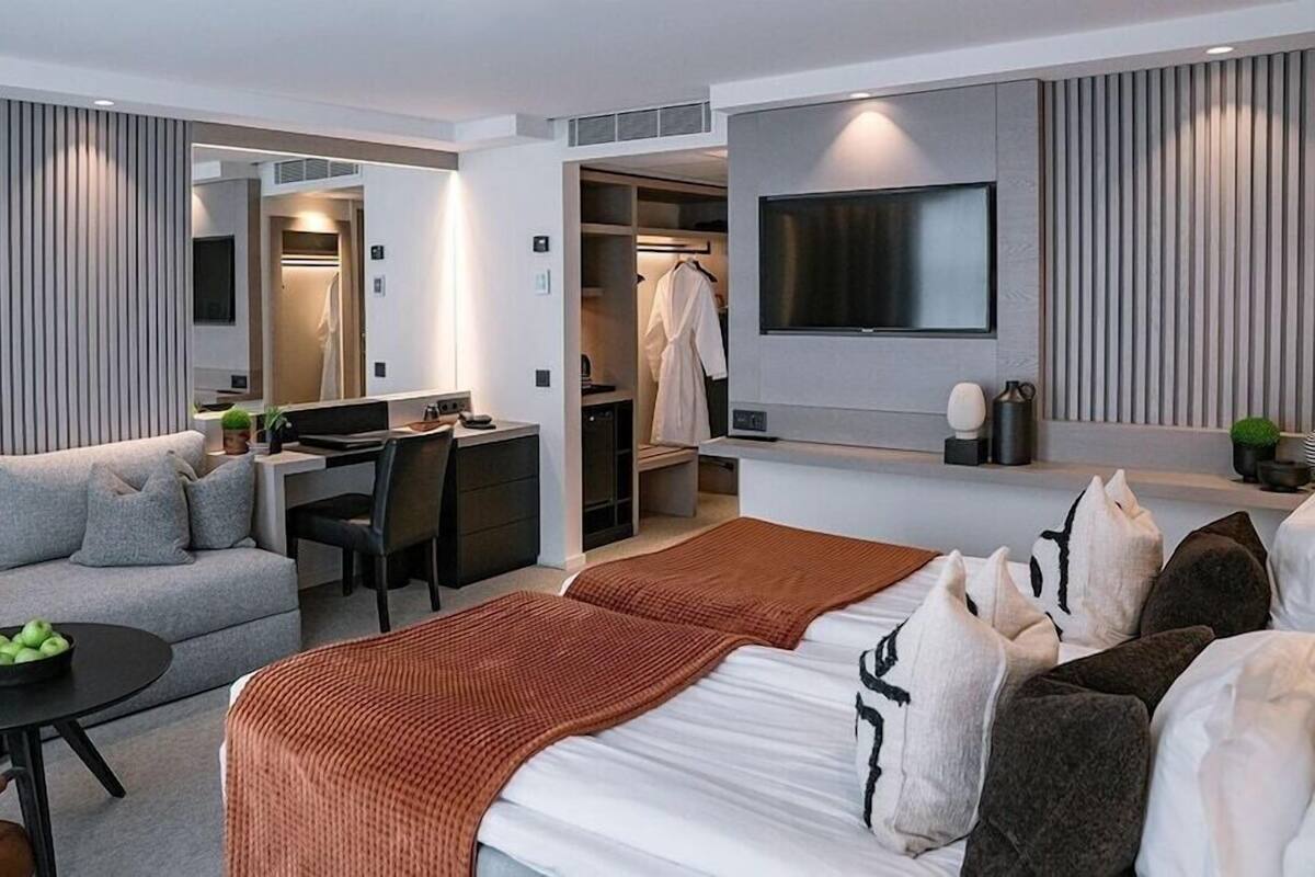 A modern hotel room with a sofa, a bed, a desk, and a TV.