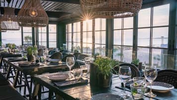 Un restaurante con mesas dispuestas para comer, ventanas amplias y lámparas de mimbre colgantes.