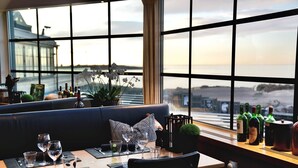 A restaurant with a view of the sea, a black leather booth, wine glasses, and bottles on the windowsill. - Hotel Tylösand (Halmstad)
