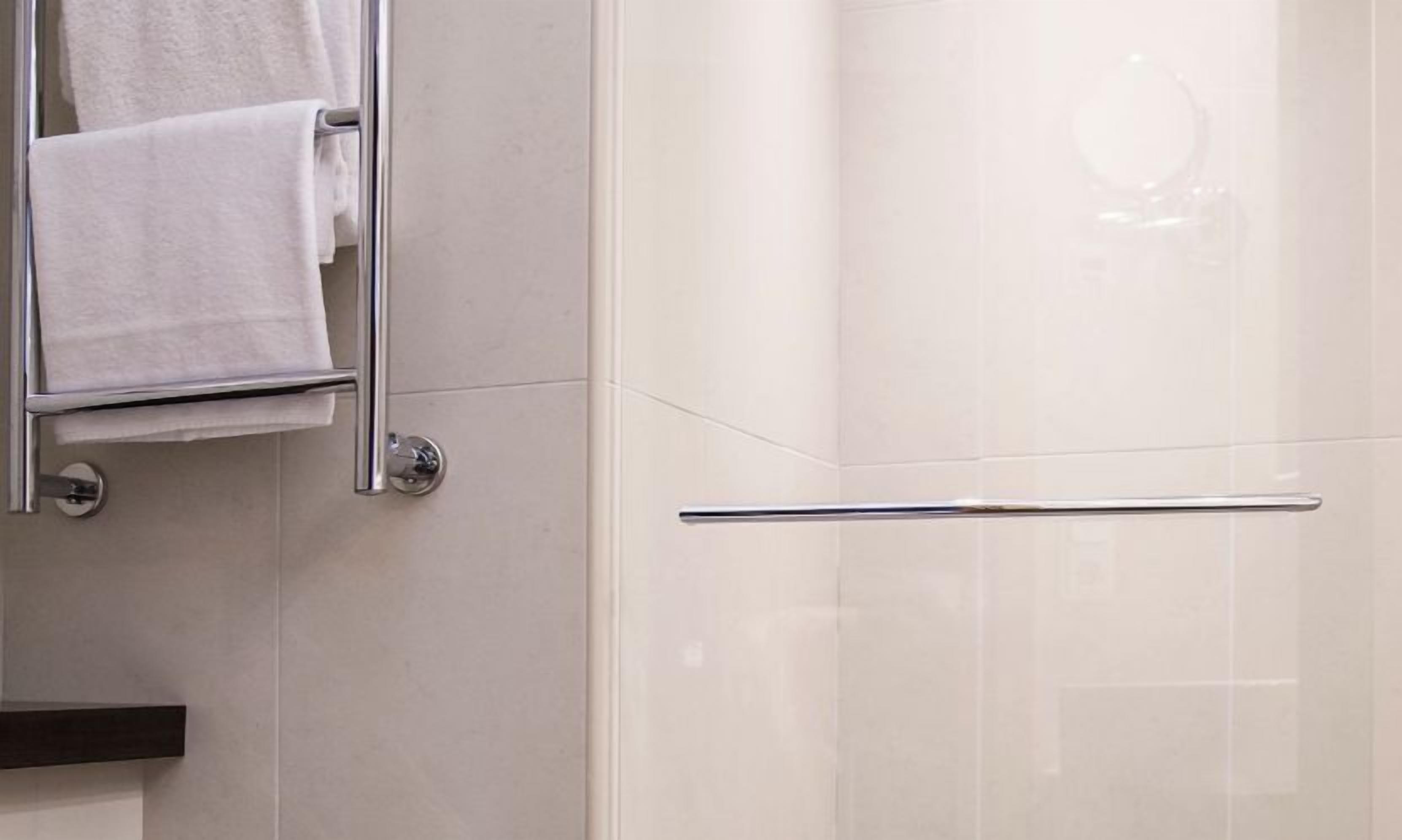 Een badkamer met een handdoekrek, een douchecabine van glas en een spiegel.