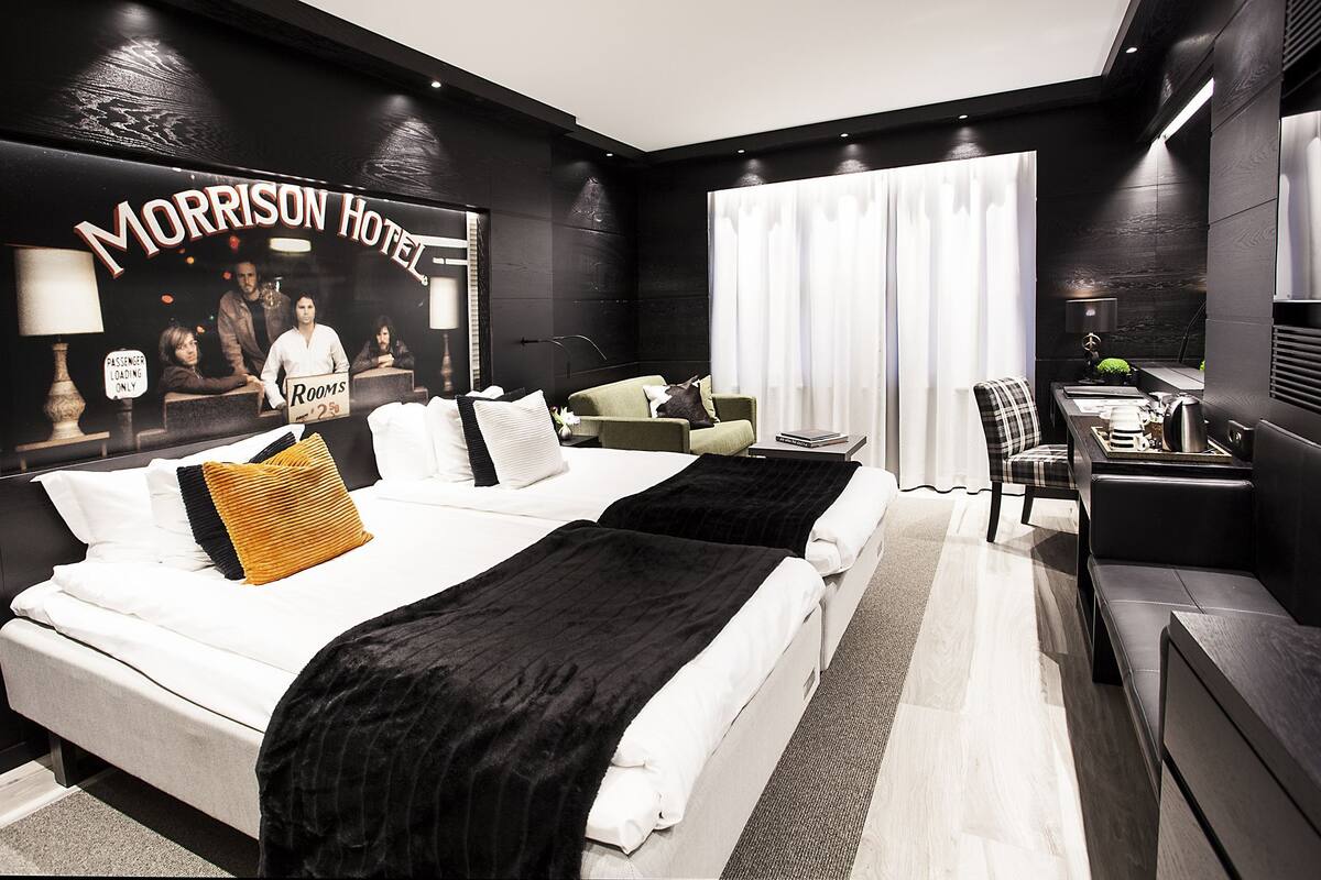 A modern hotel room with two beds, a desk, a chair, and a large poster on the wall.