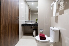 Une salle de bain moderne avec une porte en bois, un lavabo sur un plan de travail noir, des toilettes blanches et une poubelle.