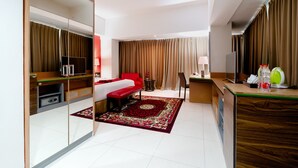 A hotel room with a bed, a desk, a mirror, a TV, and a bathroom. - Atrium Premiere Hotel (Yogyakarta)
