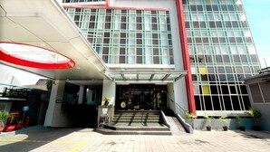 A modern building with a glass facade, a red and white entrance, and a covered area with steps leading to the entrance. - Atrium Premiere Hotel (Yogyakarta)