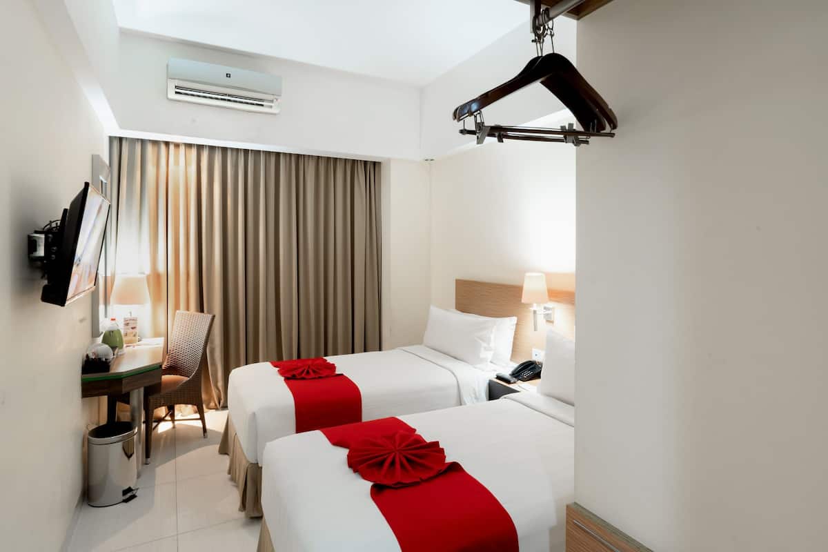 A hotel room with two beds, a desk, a chair, a TV, and a wardrobe.