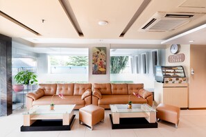 Un intérieur moderne avec un canapé en cuir, des tables basses en verre, un présentoir à pâtisseries et une grande fenêtre offrant une vue dégagée.