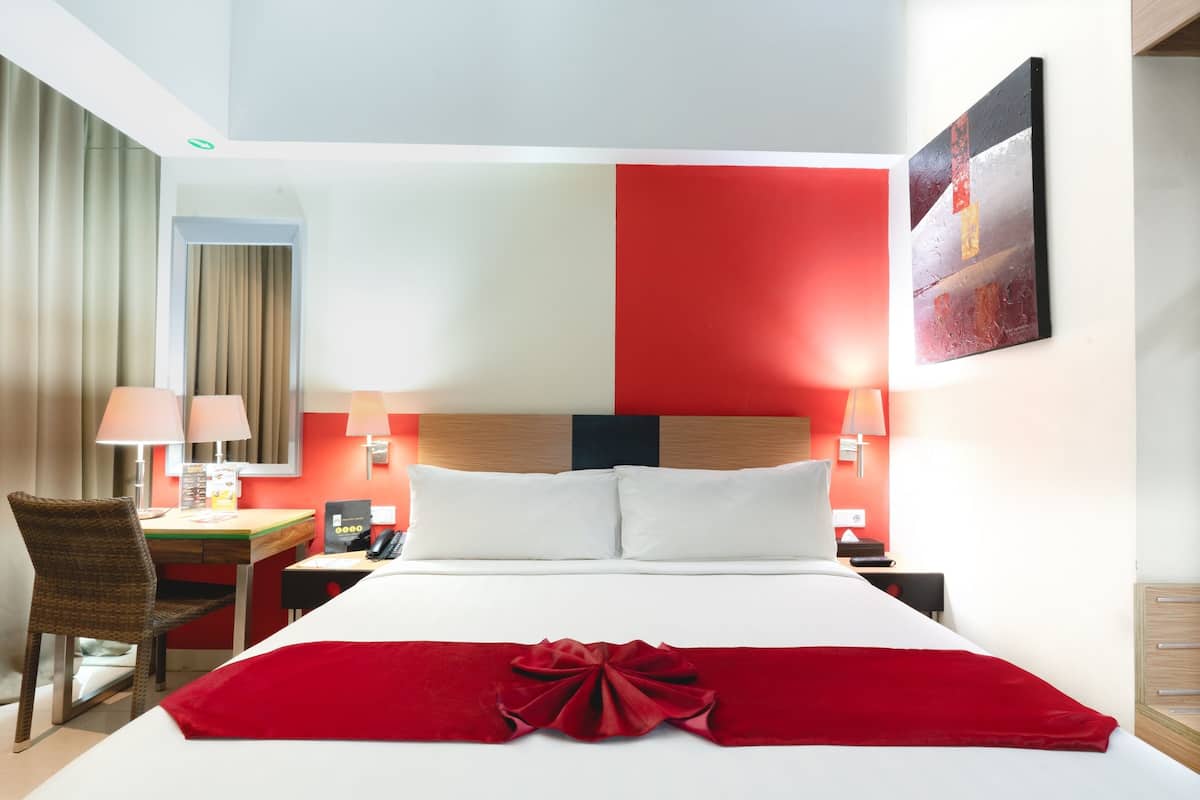 A hotel room with a bed, two bedside tables, a desk, a chair, and a wall-mounted artwork.