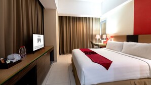 A hotel room with a bed, a desk with a TV, a chair, and a table with lamps. - Atrium Premiere Hotel (Yogyakarta)