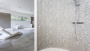 Um banheiro moderno com parede de chuveiro em mosaico, uma janela ampla e uma banheira branca.