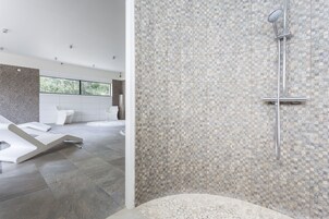 Um banheiro moderno com parede de chuveiro em mosaico, uma janela ampla e uma banheira branca.