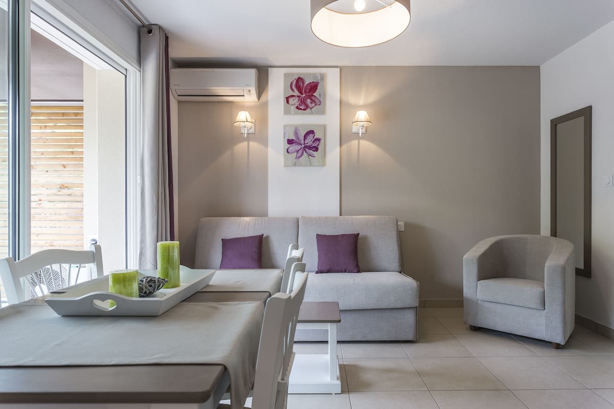 A modern living room with a sofa, armchairs, a dining table, and wall-mounted lights.