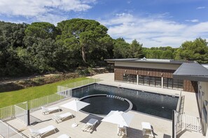 A swimming pool with lounge chairs and umbrellas, surrounded by a brick building and a grassy area with trees. - Residhotel – Résidence Pont du Gard (Remoulins)