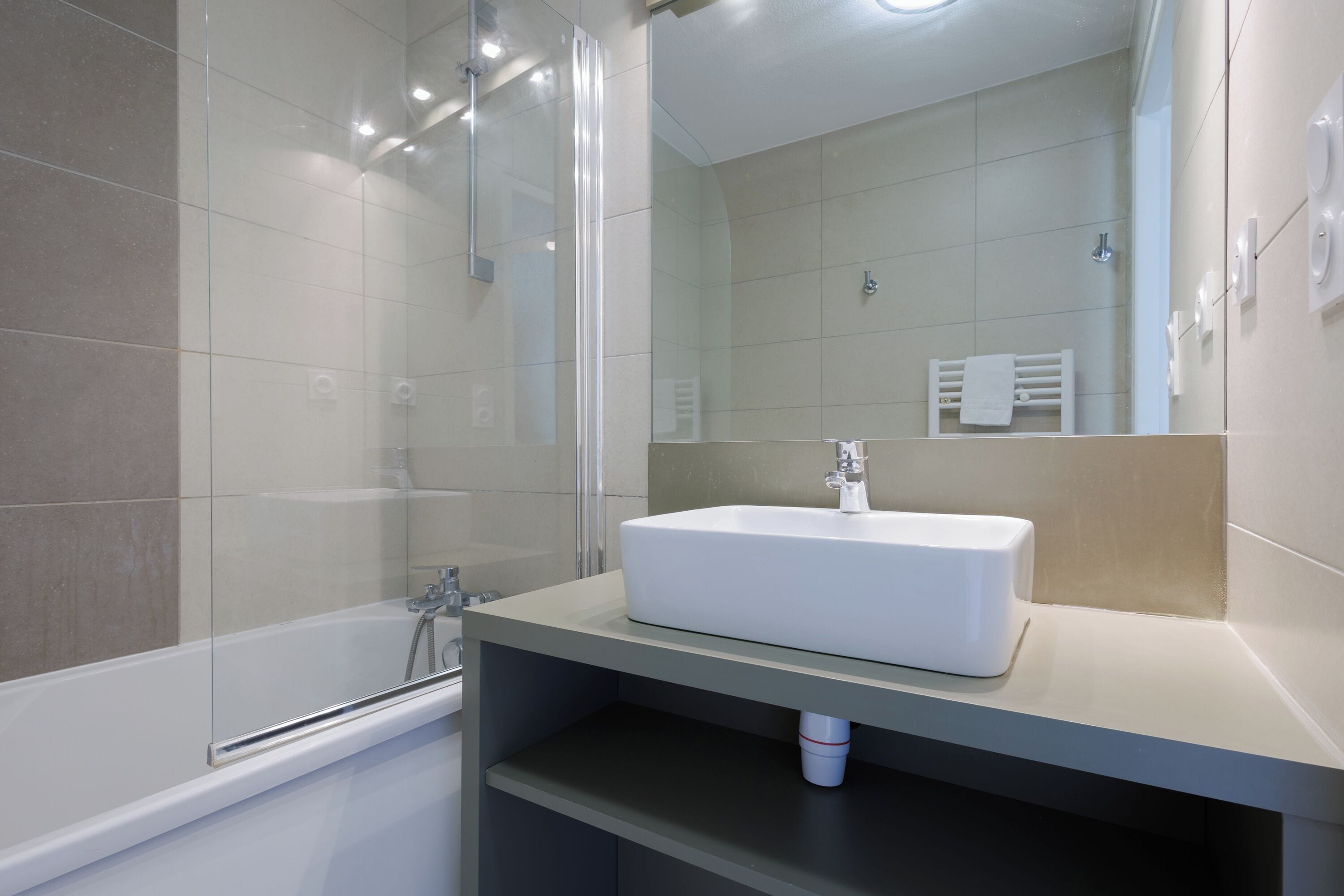 A modern bathroom with a glass-enclosed shower, a white sink, and a towel rack.