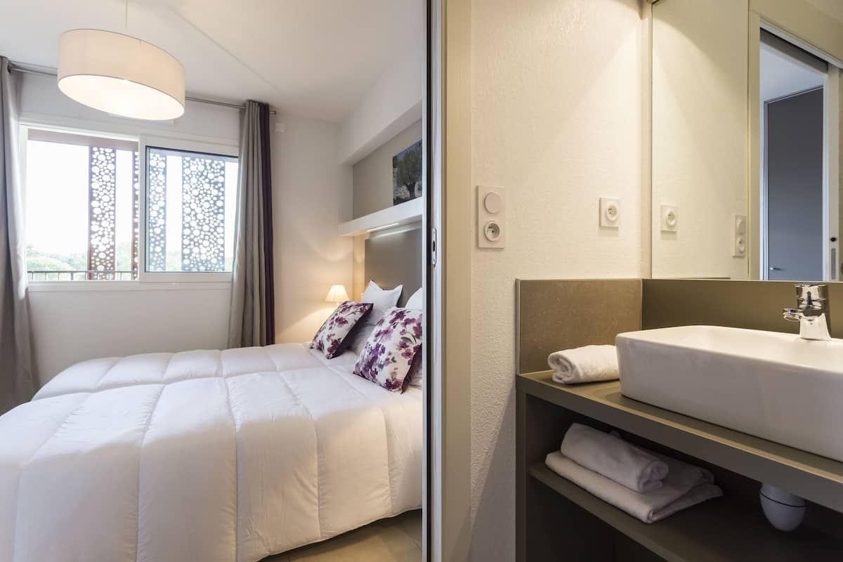 A modern hotel room with a large bed, a bedside table with a white sink, and a large mirror.