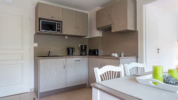 Een compacte keuken met lichte houten kastjes, een magnetron, een koffiezetapparaat en een eettafel met stoelen.