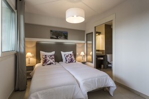 A double bed with two pillows, a bedside table with a lamp, a headboard, a painting above the bed, and a bathroom visible through an open door. - Residhotel – Résidence Pont du Gard (Remoulins)