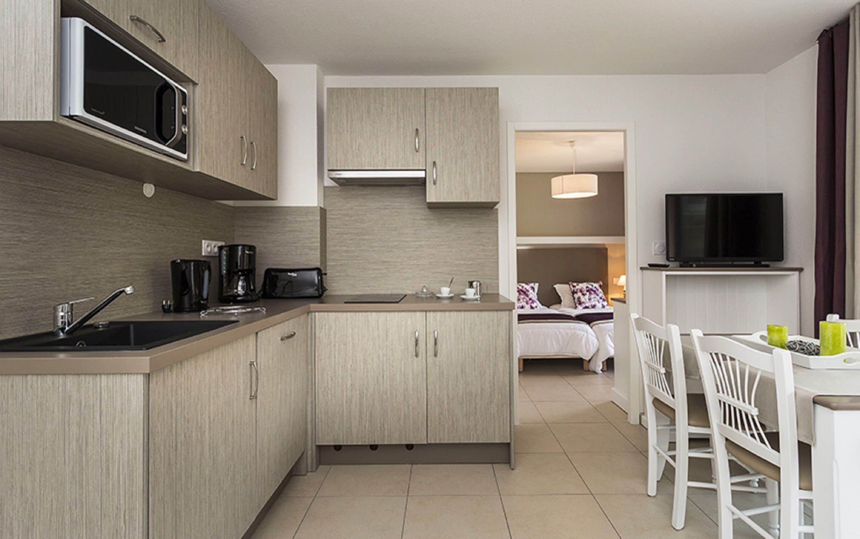 A modern kitchen with a microwave, coffee maker, and toaster. There is a dining area with a table and chairs, and a TV mounted on the wall.