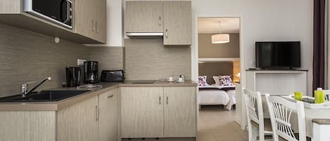 Una cocina moderna con microondas, cafetera y tostadora. Hay una zona de comedor con mesa y sillas, y un televisor montado en la pared.